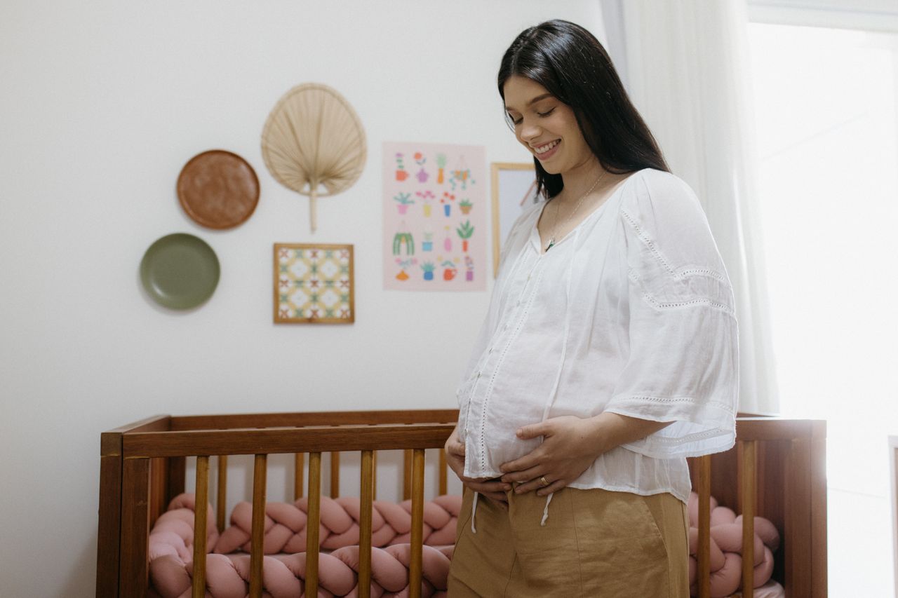 Expectant mother smiling in a cozy nursery with crib and wall decor.