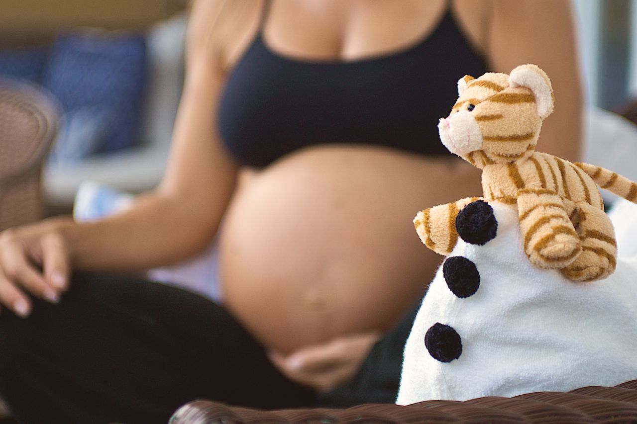 Pregnant woman sitting with a baby toy on blanket, symbolizing motherhood and upcoming birth.