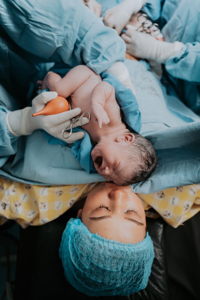 Newborn baby held by medical staff beside mother post-delivery in Mexican hospital.