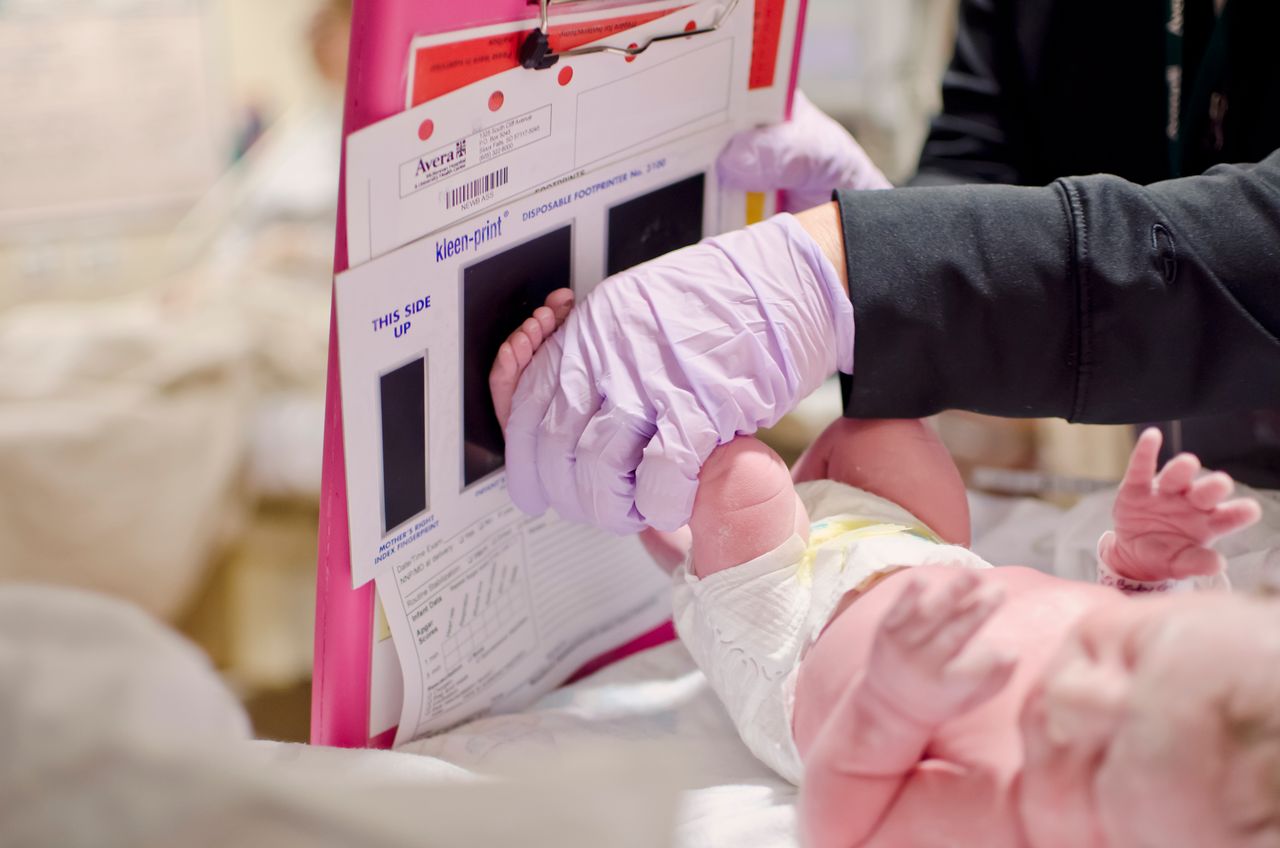 A newborn baby gets a footprint taken by a nurse in a hospital setting.