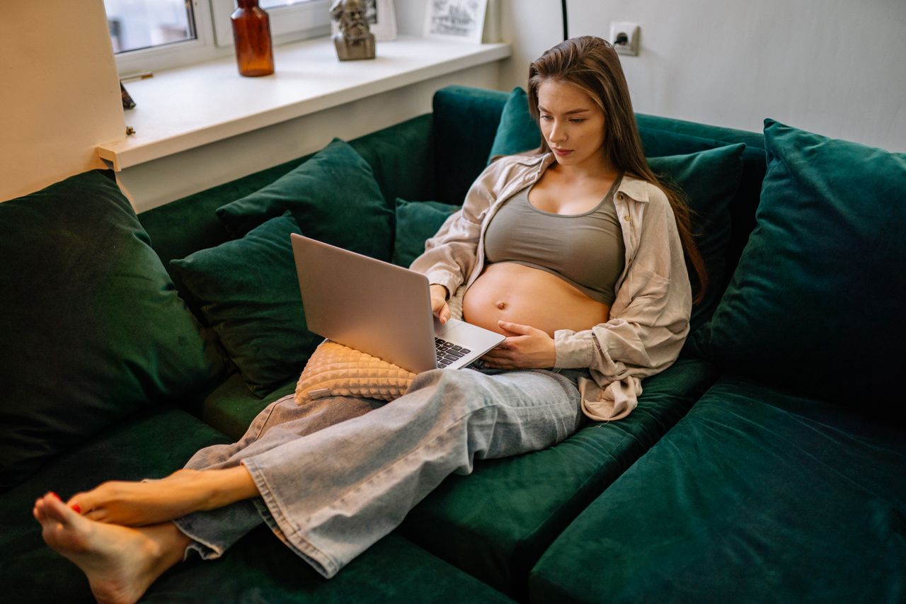 Expectant mother working from home in cozy setting with a laptop.